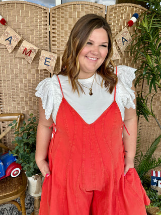 Red denim romper with white eyelet ruffle sleeves and V-neckline, styled casually.