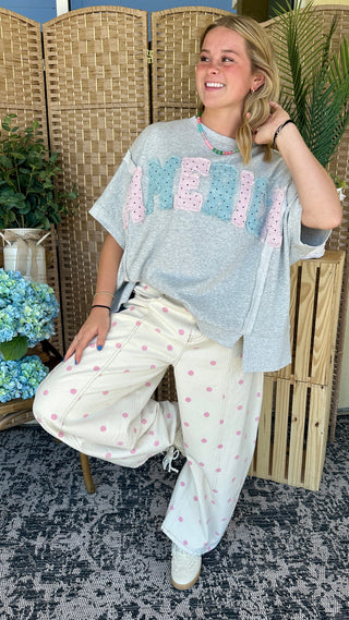 Gray t-shirt with pink and blue geometric squares graphic, styled with cream polka dot pants.
