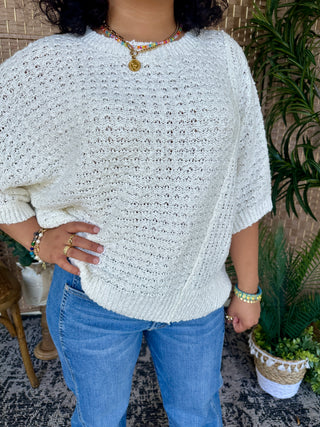Cream knit sweater with openwork pattern and asymmetrical hem, short sleeves, crew neckline.
