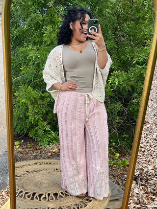Pink textured wide-leg pants with geometric pattern, worn with cream knit cardigan and beige tank top.
