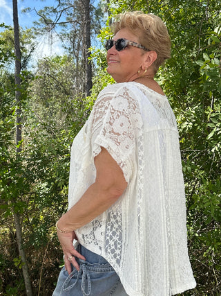 White lace handkerchief hem top with short sleeves and ornate floral pattern detailing.
