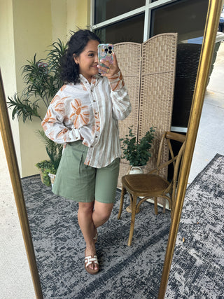 White and orange floral stripe button-down top with long sleeves on model.
