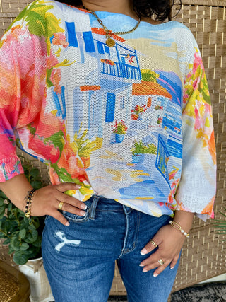 Colorful batwing top with harbor scene print in blue, pink, yellow and orange featuring boats and buildings on textured fabri
