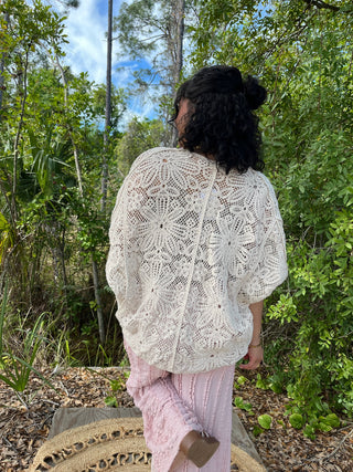 Cream crochet shrug with intricate lace pattern and three-quarter sleeves worn over pink pants.
