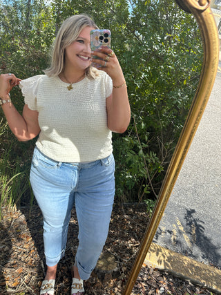 Cream textured short-sleeve top with ruched cap sleeves and crew neckline.
