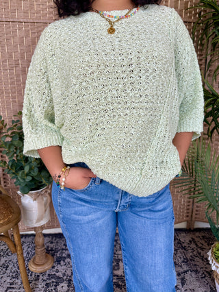 Cream knit sweater with openwork pattern and asymmetrical hemline, three-quarter sleeves.
