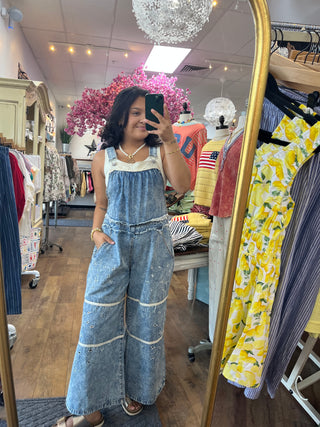 Light blue denim overalls with ivory eyelet trim and wide legs on model in boutique.
