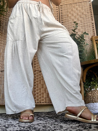 White linen wide-leg pants with drawstring waist, relaxed fit, worn with tan slide sandals.
