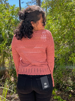 Terracotta knit cardigan with openwork pattern and scalloped hem, worn with black pants.
