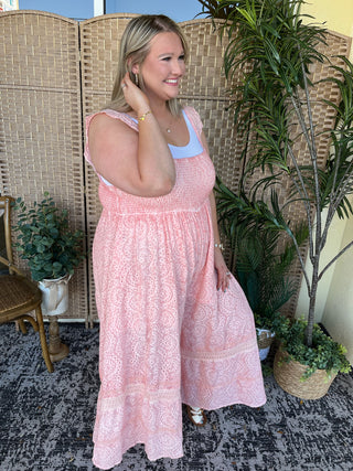 Pink eyelet jumpsuit with smocked bodice and wide-leg silhouette, layered over white tank top.
