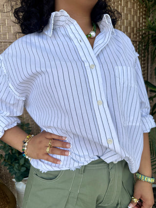 White pinstriped button-up shirt with ruched sleeves and relaxed fit worn with sage green pants.
