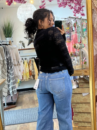 Black lace long-sleeve layering top with textured pattern, shown from back on model with light blue jeans.
