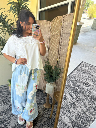 Light blue denim jogger pants with white floral and decorative patch appliqués throughout.
