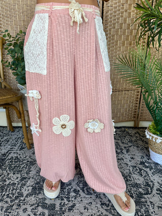 Blush pink ribbed joggers with white lace pockets, floral appliqués, and drawstring waist.