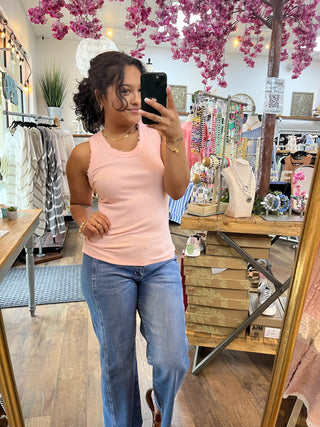 Blush pink ribbed knit sleeveless tank top on model styled with blue jeans.
