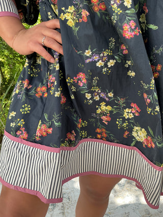 Dark navy floral dress with a contrast hem and band, featuring a feminine silhouette and flowing fabric.
