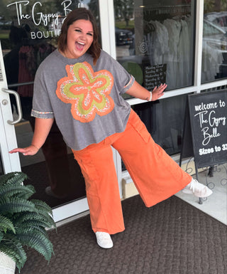 Alt text: "Mineral washed blue short sleeve top with vibrant orange flower patch, perfect for a casual, boho-chic look.