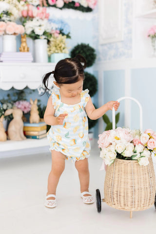 White infant romper with yellow lemon print and ruffled sleeves.

