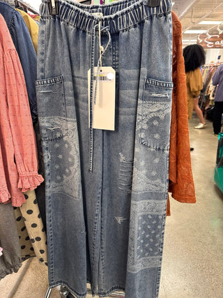 Washed blue denim wide-leg pants with distressed patchwork panels and drawstring waist on hanger.
