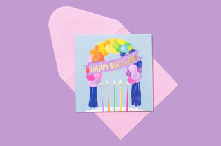 Birthday greeting card with colorful balloons, candles, and "Happy Birthday" text on light blue background.

