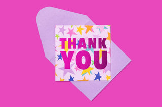 Colorful thank you greeting card with pink text and star design on lavender envelope against bright pink background.
