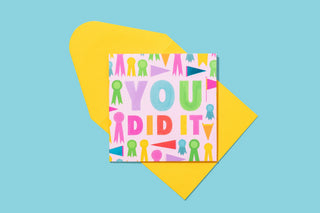 Colorful "You Did It" greeting card with multicolored text and confetti design on yellow geometric background.
