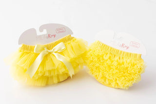 Bright yellow ruffle tutu bloomers with layered tulle and white bow detail displayed on packaging.
