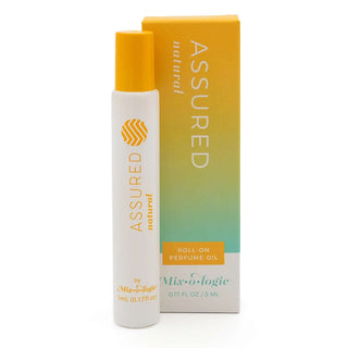ASSURED Natural Mixologie Rollerball Perfume - Elegant glass bottle with sleek black cap, surrounded by vibrant tropical leaves.